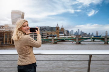 Portrait einer glücklichen, blonden Touristin in London beim Fotografieren der Skyline auf ihrer...