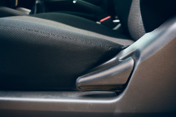 the seat level adjust button beside the black and grey  velvet seat in the car