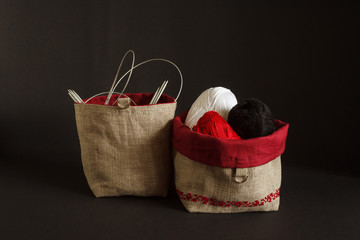 Bag for things with embroidery red ornament. Made of linen fabric. Knitting needles and threads are in the bag. Black background