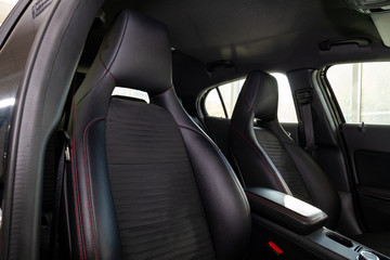 Close-up on the front sport car seats with black leather trim, lateral support and fabric inserts, of used vehicle in after detailing and dry cleaning. Auto service industry.