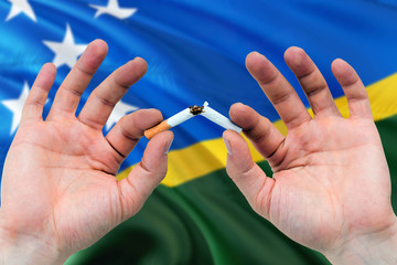 Solomon Islands quit smoking cigarettes concept. Adult man hands breaking cigarette. National health theme and country flag background.