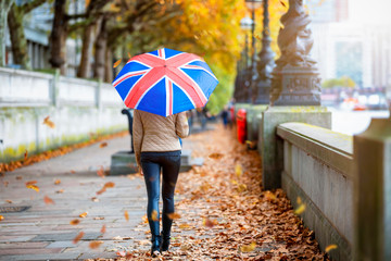 London im Herbst: Frau mit Regenschirm mit Britischer Fahne läuft am Ufer der Themse uner herbstlichen Bäumen und goldenem Laub