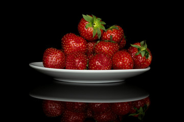 Lot of whole fresh red strawberry heap on white ceramic plate isolated on black glass