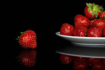 Lot of whole fresh red strawberry on white ceramic plate isolated on black glass