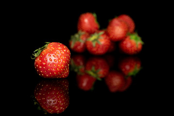 Group of seven whole fresh red strawberry one in focus isolated on black glass