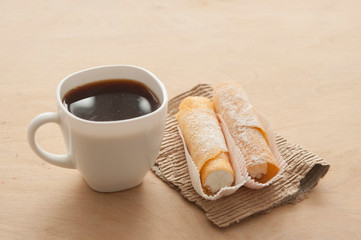Sweet snack with coffee and waffle tubes on wood background