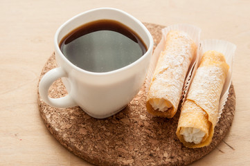 Sweet snack with coffee and waffle tubes on wood background