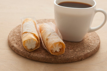 Sweet snack with coffee and waffle tubes on wood background