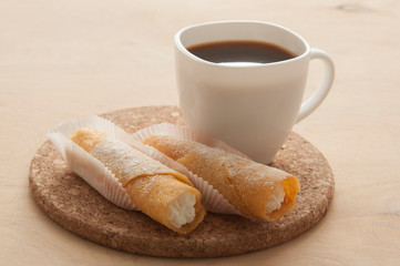 Sweet snack with coffee and waffle tubes on wood background