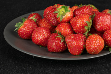 Lot of whole fresh red strawberry on gray ceramic plate on grey stone