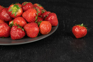 Lot of whole fresh red strawberry on gray ceramic plate on grey stone