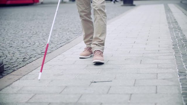 Midsection of blind man with white cane walking on pavement in city.