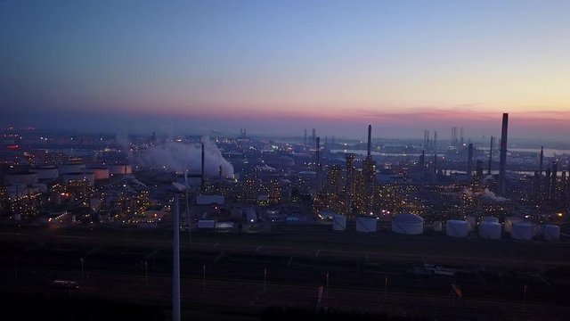 Aerial view of twilight of oil refinery , shot with drone. Oil refinery and Petrochemical plant at dusk . Wind mill visible. Shot in Pernis Rotterdam.