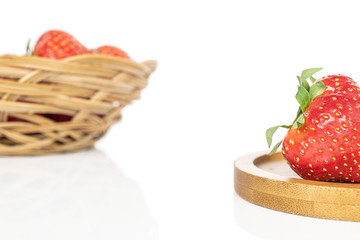 Lot of whole fresh red strawberry in round rattan bowl on round bamboo coaster isolated on white background