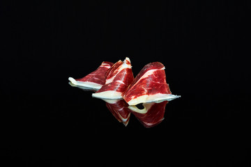 studio photo of a series of slices of 100% Iberian acorn-fed ham folded on black background with...