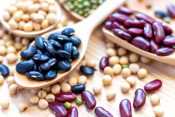 Many types of beans are separated in a spoon on a wood table such as mung bean, soybean, black bean, red bean. Leguminous plant native to Asia, widely cultivated for its edible seeds.