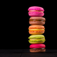 Stack of french colorful macaroons on wooden table isolated on black background