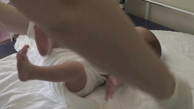 Close up hands in surgical gloves of nurse while changing diapers newborn baby on table in hospital room.