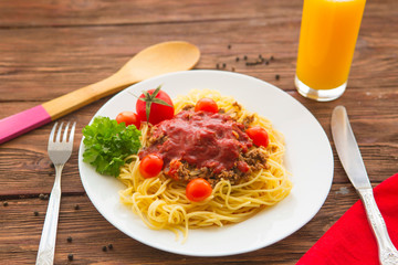 Bowl of spaghetti bolognese with tomatoes on wooden table in background