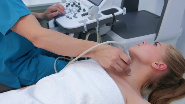 Ultrasound scanning diagnostic for young woman of thyroid gland in clinic. Doctor runs ultrasound sensor over patient's neck. Examination in clinic for diagnostic, making diagnosis.