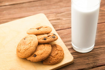 Chocolate chip cookies with milk in glass on rustic wooden table