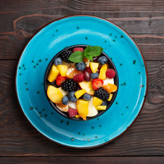 Bowl of healthy fresh fruit salad on dark wooden background. Selective focus, top view.