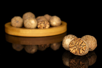 Group of lot of whole one half one piece of dry brown nutmeg on bamboo coaster isolated on black glass
