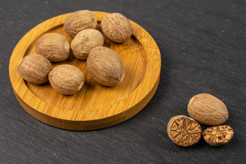 Group of eight whole one half one piece of dry brown nutmeg on bamboo coaster on grey stone