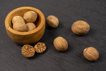 Group of eight whole one half one piece of dry brown nutmeg in tiny wooden bowl on grey stone