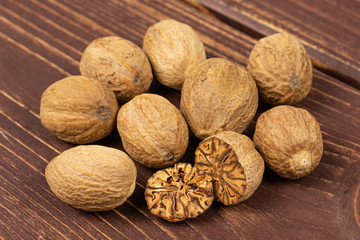 Group of eight whole one half one piece of dry brown nutmeg on brown wood