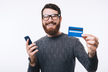 Happy handsome man with eyeglasses showing his new credit card an holding smartphone