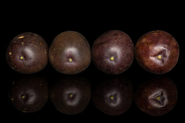 Group of four whole sweet dark purple passion fruit isolated on black glass