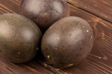 Group of three whole sweet dark purple passion fruit on brown wood