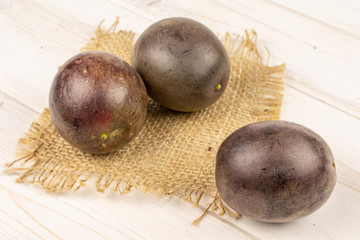 Group of three whole sweet dark purple passion fruit on natural sackcloth on white wood