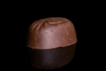 One whole dark brown delicious chocolate praline isolated on black glass