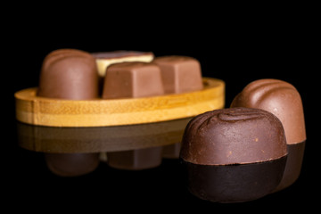 Group of six whole delicious chocolate praline on bamboo coaster isolated on black glass