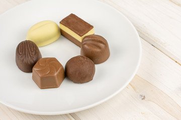 Group of six whole delicious chocolate praline on white ceramic plate on white wood