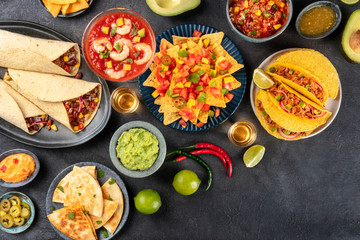 Mexican food, many dishes of the cuisine of Mexico, flat lay, overhead shot on a black background with copy space. Nachos, tequila, guacamole, burritos, quesadillas, tacos
