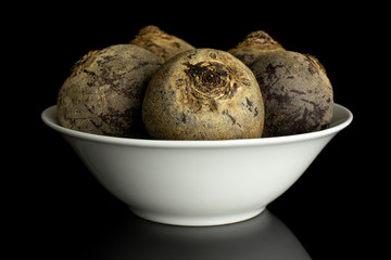 Group of five whole raw red beetroot in white ceramic bowl isolated on black glass