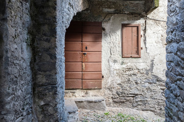 Fototapeta na wymiar Closed wooden door and a window in a narrow street of a Piedmontese village