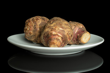 Group of three whole fresh brown jerusalem artichoke on white ceramic plate isolated on black glass