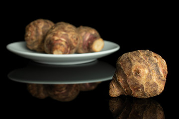 Group of four whole fresh brown jerusalem artichoke on white ceramic plate isolated on black glass