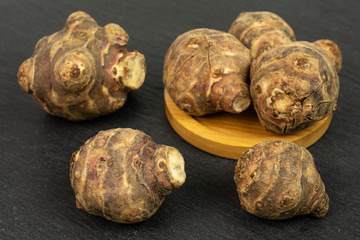 Group of six whole fresh brown jerusalem artichoke on bamboo coaster on grey stone