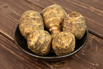 Group of five whole fresh brown jerusalem artichoke in dark ceramic bowl on brown wood