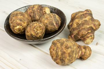 Group of six whole fresh brown jerusalem artichoke in dark ceramic bowl on white wood