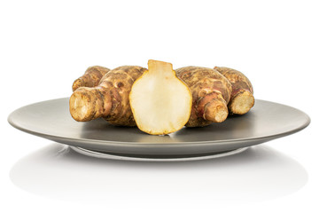 Group of four whole one half of fresh brown jerusalem artichoke on gray ceramic plate isolated on white background