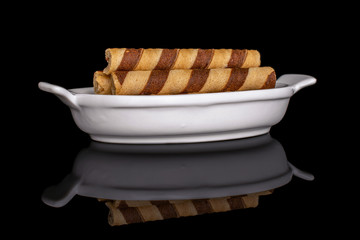 Group of three whole crunchy beige hazelnut rolled wafer biscuit in white oval ceramic bowl isolated on black glass