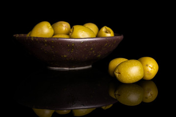 Lot of whole pitted green olive in dark ceramic bowl isolated on black glass