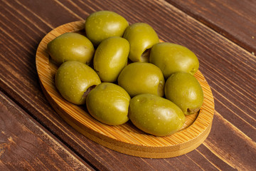 Lot of whole pitted green olive on bamboo coaster on brown wood