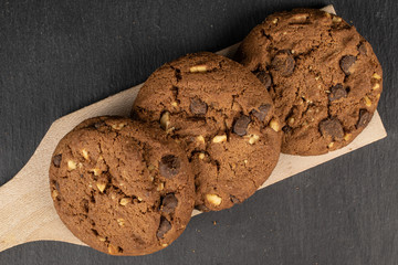 Group of three whole sweet brown cookie on wooden cutting board flatlay on grey stone